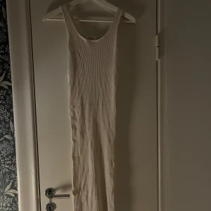 Vit ribbad långklänning - Snygg vit ribbad långklänning med smala axelband. Perfekt för en stilren och enkel look. Klänningen har en kroppsnära passform som framhäver figuren.
