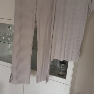Beige ribbade byxor med matchande topp set  - Säljer ett set med beige ribbade byxor och en matchande topp. Byxorna har en loose passform och är tillverkade i ett mjukt material. Toppen har korta ärmar och en rund halsringning. Perfekt för en avslappnad look. Set 