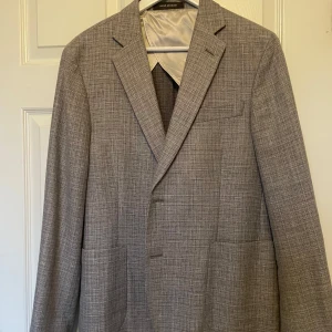 Grå kavaj från Oscar Jacobson - Snygg grå kavaj från Oscar Jacobson, perfekt för stilrena tillfällen. Kavajen har en klassisk design med två knappar och ett diskret rutmönster. Tillverkad i ett lätt och bekvämt material som passar bra för både vår och sommar.