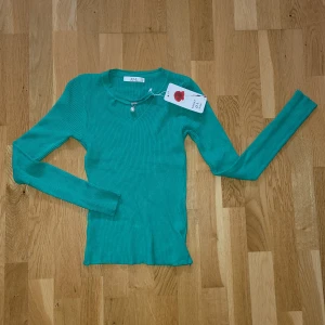 Grön ribbad tröja från JJ-L - Helt ny grön ribbad tröja från JJ-L med en dekorativ pärldetalj vid halsen. Tröjan har långa ärmar och en figurnära passform, perfekt för att lägga till lite färg i garderoben. Lappen sitter kvar. Passar mig som har S. Köparen står för frakten 💚