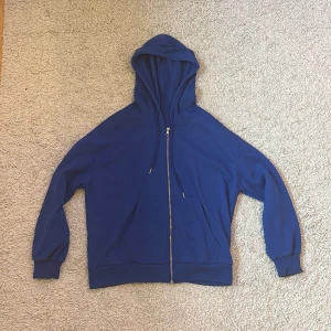 Blå hoodie med dragkedja - Säljer en snygg blå hoodie med dragkedja och huva. Tröjan har långa ärmar och en praktisk ficka framtill. Perfekt för en avslappnad stil.