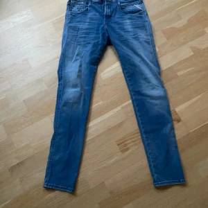 Blå jeans från Replay - Snygga blå jeans från Replay i modellen Anbass. De har en slim fit passform och är tillverkade i ett bekvämt jeansmaterial. Byxorna har klassisk femficksdesign och en dragkedja framtill. Perfekta för en stilren look.