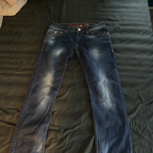 Blå jeans från Emporio Armani - Snygga blå jeans från Emporio Armani med coola slitningar och broderad detalj på bakfickan. De har en klassisk femficksdesign och en läderpatch med logotyp baktill. Perfekta för en stilren look.