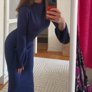 Blå långklänning med vida ärmar - Snygg blå långklänning med vida ärmar och en elegant passform. Perfekt för att sticka ut med sin unika struktur och stilrena design. Klänningen har en vacker mörkblå färg som passar till många tillfällen.