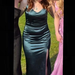 Mörkgrön balklänning med spetsdetaljer - Mörkgrön balklänning i satin med v-ringad hals och smala axelband. Klänningen har en vacker spetsdetalj på ryggen och en slits framtill. Dragkedja i sidan. Endast använd en kväll! Uppsydd efter mig som är 160cm.  Nypris: 1099kr 💚Skriv gärna vid önskan om fler bilder eller mått!