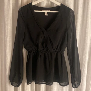 Svart blus - Snygg svart blus med lite genomskinliga ärmar och en elegant v-ringning. Perfekt för en stilren look. Blusen har en smickrande passform och är lätt att matcha med olika outfits. Inga defekter