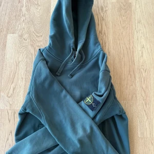 Grön hoodie från Stone Island - Säljer en snygg grön hoodie från Stone Island med klassisk logga på ärmen. Tröjan har en bekväm passform med långa ärmar och en praktisk magficka. Perfekt för en avslappnad stil. Äkta och bra skick hör av er🤠