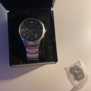 Silverfärgad klocka från Emporio Armani - Snygg och stilren klocka från Emporio Armani med silverfärgad länk och mörkblåaktig urtavla. Box och externa länkdelar som tagits av tillkommer. Nypris ca 2200