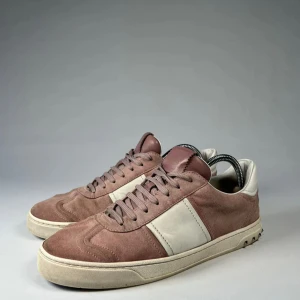 Rosa Valentino Fly Crews - Snygga sneakers i rosa mocka med vita skinnpaneler från Valentino. Skorna har snörning och en bekväm sula. Perfekta för en stilren look. Skick: 3/5