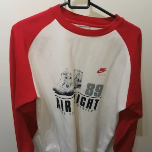 Vit och röd tröja från Nike - Säljer en cool vit och röd tröja från Nike med tryck av sneakers och texten 'Air Flight 89'. Tröjan har långa ärmar och en rund halsringning. Perfekt för dig som gillar retrostil och sportiga vibbar. 🏀