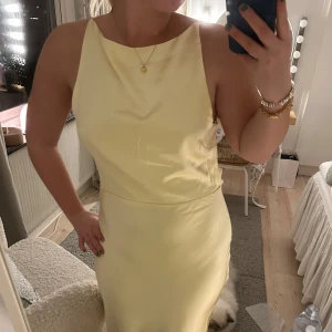 Gul maxiklänning - Elegant champagnefärgad långklänning i satin med en öppen rygg och smala axelband. Klänningen har en figurnära passform och en stilren design som ger en lyxig känsla. Perfekt för speciella tillfällen. Jag säljer den på grund av att jag har skolios, vilket gjorde att axelbanden inte höll uppe då min rygg går ut mer än vanligt runt axeln🥰