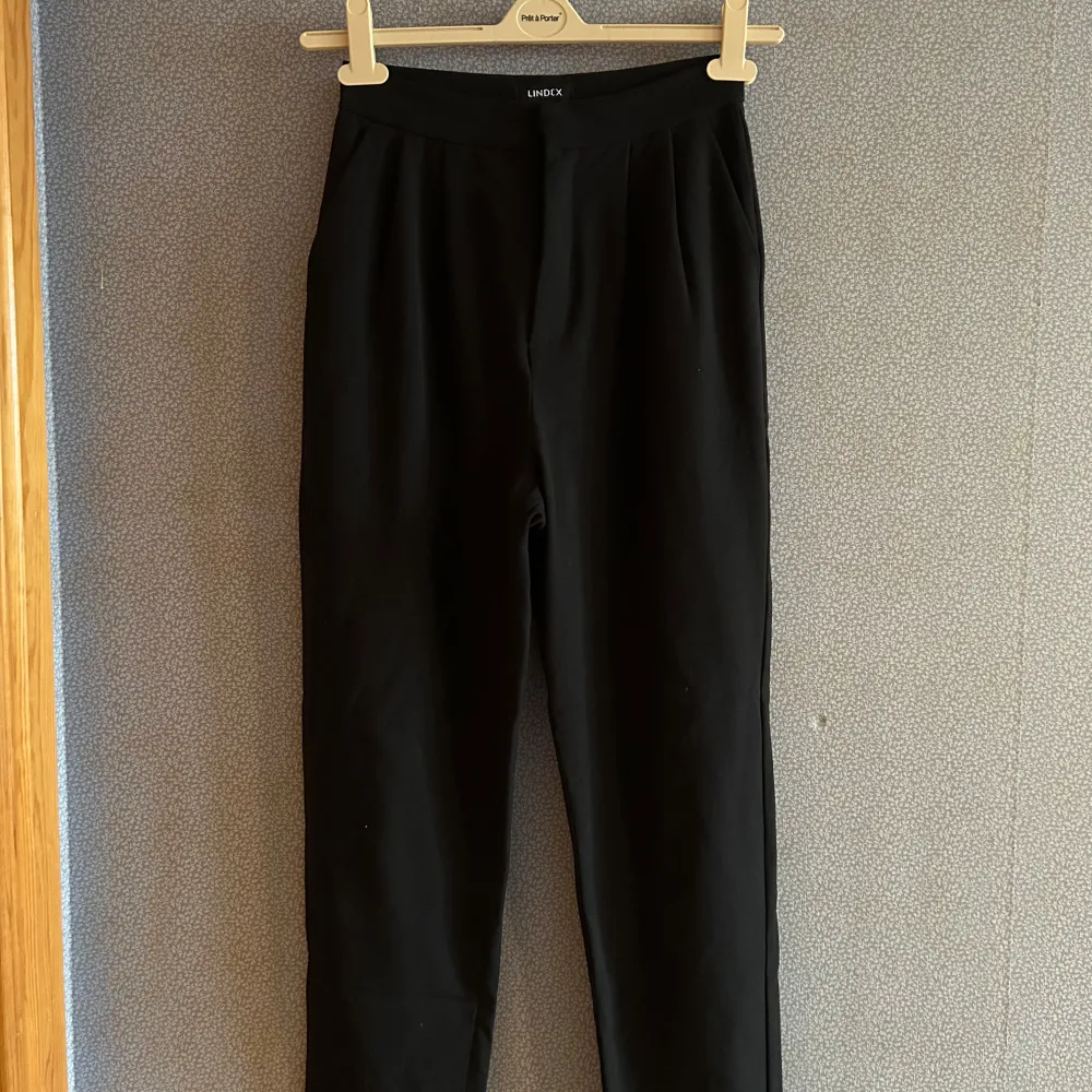 Snygga svarta kostymbyxor från Lindex i en stilren design. Byxorna har en elastisk midja och en bakficka. Perfekta för en chic och bekväm look.. Farkut & Housut.