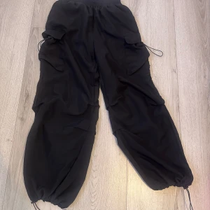 Svarta cargopants från Shein - Snygga svarta cargopants från Shein med elastisk midja och justerbara dragskor vid bensluten. Byxorna har flera praktiska fickor och en loose passform, perfekt för en avslappnad stil.