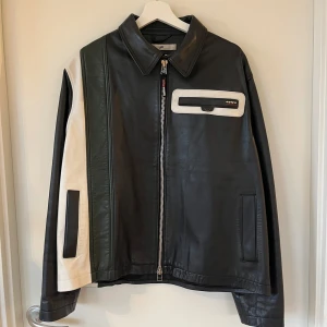 Eytys Skinnjacka - Snygg svart skinnjacka från Off-White med unika vita och gröna paneler. Jackan har en dragkedja framtill och en cool fickdetalj på bröstet. Perfekt för att ge din outfit en edgy touch.