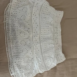 Vit spetskjol - Säljer en superfin vit spetskjol som är perfekt för sommaren! Kjolen har ett vackert broderat mönster och volanger som ger den en romantisk touch. Den är i nyskick och passar perfekt till både vardag och fest. Materialet känns lätt och luftigt, vilket gör den bekväm att bära hela dagen.