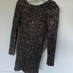 Glittrig klänning från Rebecca Stella - Säljer en superfin glittrig klänning från Rebecca Stella för Nelly. Den är i storlek S och har en snygg öppen rygg som verkligen sticker ut. Klänningen är perfekt för fest och nyår med sina långa ärmar och glittriga paljetter som täcker hela plagget. Den är i nyskick och redo att bli din nya favorit i garderoben!