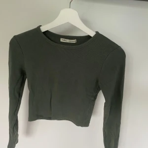 Grön ribbad tröja från Pull&Bear - Säljer en snygg grön ribbad tröja från Pull&Bear. Den är långärmad och har en croppad passform som är perfekt för både vardag och fest. Tröjan är i storlek S och är i bra skick. Perfekt för höst och vår!