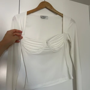 Vit långärmad topp från Chiquelle - Säljer en superfin vit långärmad topp från Chiquelle i storlek medium. Toppen har en unik design med veckade detaljer över bysten som ger en snygg look. Stretchigt material. Nypris 399.