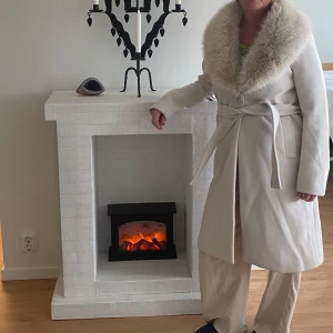 Elegant vit kappa med äkta päls - Säljer en superfin vit kappa med en lyxig pälsdetalj runt kragen. Den har ett bälte i midjan för en snygg passform och är perfekt för kyliga dagar. Kappan är långärmad och har en klassisk stil som funkar både till vardags och fest. Den är i nyskick och redo för en ny ägare!