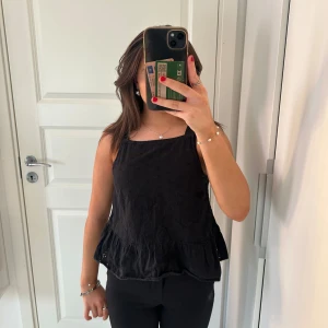 Svart ärmlös topp med volangdetalj - Nu säljer jag en supersnygg svart topp med volang i nederkanten. Toppen har ett diskret blommönster och passar för både vardag och fest. Toppen är sällan använd och är som ny! Kontakta mig om du har några frågor🥰