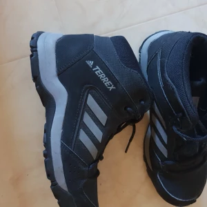 Svarta Adidas Terrex sneakers - Säljer ett par svarta Adidas Terrex sneakers i bra skick. De har en robust design med snörning och de klassiska tre ränderna på sidan. Perfekta för utomhusaktiviteter och äventyr.