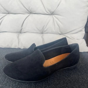 Svarta loafers i mocka - Säljer ett par stilrena svarta loafers i mocka. De är i bra skick och perfekta för både vardag och fest. Skorna har en bekväm passform och en diskret design som passar till det mesta. 