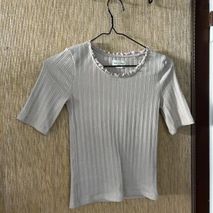 Beige ribbad topp från Holly & Whyte - Säljer en superfin beige ribbad topp från Holly & Whyte. Den har en söt volangdetalj runt halsringningen och trekvartsärmar. Perfekt för både vardag och fest! 🥰