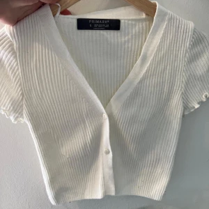 Vit ribbad kortärmad topp från Primark - Säljer en superfin vit ribbad topp från Primark. Den har korta ärmar och knappar framtill, vilket ger en snygg och stilren look. Perfekt för både vardag och fest!