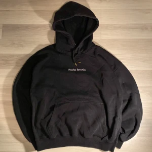 Svart hoodie från District Fortysix - Säljer en svart hoodie från District Fortysix i storlek S men passar mer som M. Den har en cool design med en stor vit illustration på baksidan och texten 'district fortysix' broderad på framsidan. Hoodien är i bomull och har en klassisk känguruficka samt ribbade muddar vid ärmslut och nederkant. Perfekt för höst och vinter! Hör av dig om du har några frågor!
