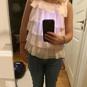 Rosa volangblus - Säljer en söt rosa blus med flera lager av volanger. Blusen är ärmlös och har en luftig passform, perfekt för varmare dagar. Den är gjord i ett lätt och bekvämt material.