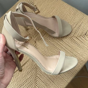 Beige sandaler med klack - Eleganta beige sandaler med klack och öppen tå. De har en smal rem över tårna och en justerbar rem runt ankeln med ett guldfärgat spänne. Använda endast i någon timme inomhus, storlek 37💌