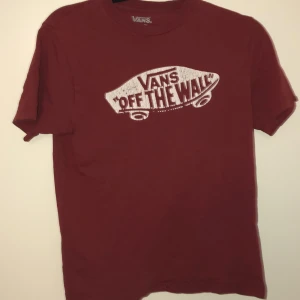 Röd t-shirt från Vans - Säljer en röd t-shirt från Vans med det klassiska 'Off The Wall'-trycket på framsidan. T-shirten är tillverkad i 100% bomull och har en normal passform. Perfekt för en avslappnad stil. Stl M= 146 cm