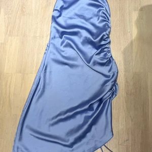 Ljusblå sidenklänning från NA-KD - Säljer en ljusblå klänning från NA-KD i sidenmaterial. Klänningen har en omlott-design med snörning i ryggen och sne skurning nedtill.