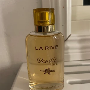 La Rive Vanilla Touch Eau de Parfum - Säljer en flaska La Rive Vanilla Touch Eau de Parfum. Flaskan är genomskinlig med en gyllene vätska och har en guldfärgad kork. Doften har en söt och varm vaniljton, perfekt för dig som älskar mjuka och inbjudande dofter. Flaskan har en elegant design med en vaniljblomma på etiketten. Har tyvärr inte kvar förpackningen ❤️