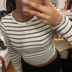 Randig ribbad tröja - Säljer en stilren vit och svart randig ribbad tröja med långa ärmar. Perfekt för en avslappnad look. Tröjan har en klassisk passform och är gjord i ett mjukt och stretchigt material.