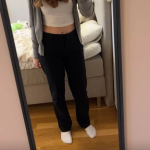 Svarta kostymbyxor från Stockh LM - Snygga svarta kostymbyxor från Stockh LM med hög midja och rak passform. Byxorna har en stilren design med en dekorativ ringdetalj vid midjan. Perfekta för en elegant look.