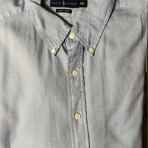 Grå skjorta från Ralph Lauren - Snygg grå skjorta från Ralph Lauren i storlek XXL. Skjortan har en klassisk design med knappar framtill och en mjuk krage. Perfekt för en stilren look.