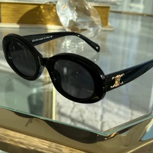 Svarta solglasögon från Céline - Snygga svarta solglasögon från Céline med ovala linser och en elegant gulddetalj på skalmarna. Perfekta för en stilren look.