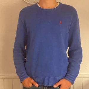 Blå tröja från Polo Ralph Lauren - Snygg blå tröja från Polo Ralph Lauren med det klassiska röda logotypbroderiet på bröstet. Tröjan har en rund halsringning och är tillverkad i ett mjukt material som ger en bekväm passform. Perfekt för en stilren look. Skriv vid fundering kring varan eller pris
