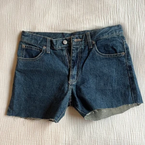 Jeansshorts med rå kant - Snygga jeansshorts i mörkblå denim med rå kant. Klassisk femficksdesign och knappgylf. Perfekta för en avslappnad stil.