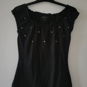 Svart topp från Ann Taylor Loft - Svart topp från Ann Taylor Loft med små dekorativa detaljer framtill. Toppen har korta ärmar och en rund halsringning. Storlek Xxs men extremt stretchig passar upp till S. 