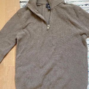 Beige stickad tröja från H&M - Säljer en stilren beige stickad tröja från H&M med dragkedja vid halsen. Tröjan har en slim fit passform och långa ärmar, perfekt för kyligare dagar. Enkelt att matcha med olika outfits.