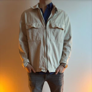 Beige overshirt med dragkedja - Säljer en stilren beige overshirt med dragkedja och två bröstfickor. Perfekt för lager-på-lager och har en avslappnad passform. Passar bra till både jeans och chinos.
