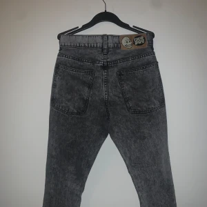 Grå jeans från Cheap Monday - Snygga grå jeans från Cheap Monday med en cool tvättad look. De har en klassisk femficksdesign och en läderlapp med logotyp baktill. Perfekta för en avslappnad stil.