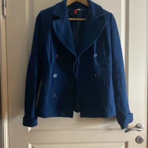 Mörkblå kappa från Divided by H&M - Säljer en stilren mörkblå kappa från Divided by H&M. Jackan har en klassisk design med knappar framtill och långa ärmar. Perfekt för höst och vår. Passar dig som gillar en normal passform.