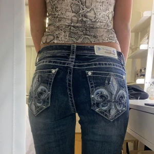 Mörkblå jeans med broderade bakfickor - Snygga mörkblå jeans från Grace (Liknar Miss Me) med unika broderade detaljer på bakfickorna. Jeansen har en klassisk femficksdesign och en bekväm passform. Perfekta för dig som vill ha något extra i garderoben! Innerbenslängden: 77cm Midjemått: 35cm  + Ursäkta dåliga kamerakvaliten!