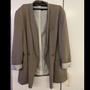 Beige kavaj - Snygg beige kavaj med normal passform och långa ärmar. Kavajen har knappar framtill och en stilren design som passar perfekt för både vardag och mer formella tillfällen.