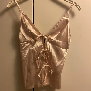 Rosa satinlinne med knytband - Snyggt rosa satinlinne med smala axelband och knytband framtill. Perfekt för en elegant look med sin glansiga finish och feminina design.