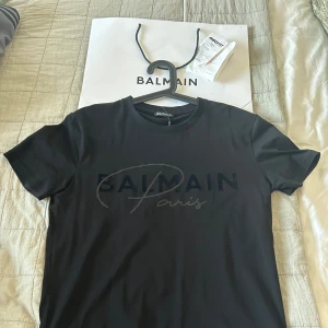 Svart t-shirt från Balmain - Priset går att diskutera!  Snygg svart t-shirt från Balmain med tryck på framsidan. Den har en klassisk rund hals och korta ärmar. Perfekt för en stilren look.