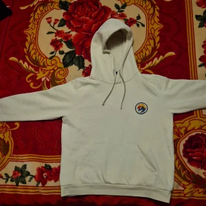 Vit hoodie från Everest - Säljer en stilren vit hoodie från Everest med en broderad logga på bröstet. Hoodien har en klassisk design med dragsko i huvan och en stor magficka. Perfekt för en avslappnad stil! 🏔️